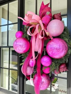 a wreath with pink ornaments hanging on the front door