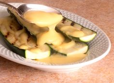 a white plate topped with sliced cucumbers covered in cheese and sauce next to a fork