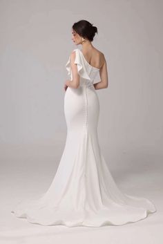 a woman in a white wedding dress with one shoulder and an open back, looking at the