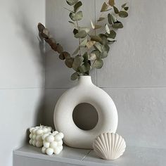 a white vase sitting on top of a shelf filled with flowers and seashells