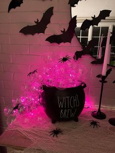 a witch's brew bucket filled with purple lights and bats next to a white brick wall