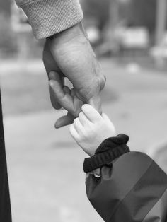 a black and white photo of a person holding the hand of a child's hand