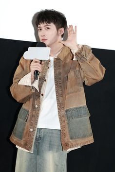 a young man holding a microphone up to his ear while standing in front of a white wall