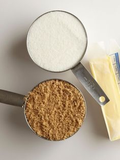 two measuring spoons filled with sugar and butter next to a cheese slice on a white surface