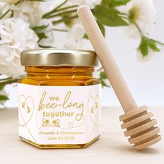 a jar of honey with a wooden spoon next to it and flowers in the background