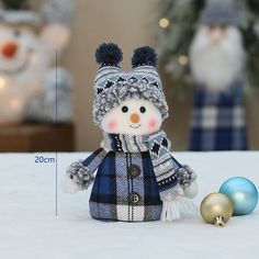 a small snowman with a hat and scarf next to two ornaments on a table