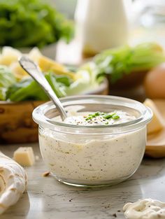 a glass bowl filled with dressing on top of a table next to vegetables and bread