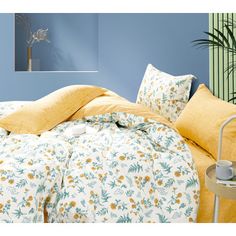 a bed with yellow and blue sheets in a room next to a potted plant