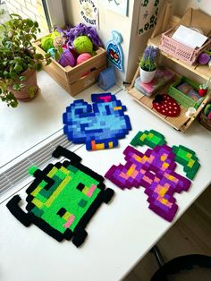 three pixel art pieces on a table in front of some plants and other items for sale