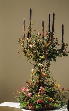 an arrangement of flowers and candles on a table in front of a beige wall with a person looking at it