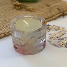 a small glass candle sitting on top of a table next to some flowers and seeds