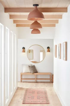 a hallway with white walls and wooden ceilinging has a round mirror on the wall