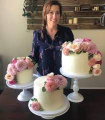 a woman standing next to three cakes with flowers on them