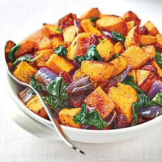 a white bowl filled with cooked vegetables on top of a table next to a fork