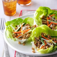 lettuce wraps filled with meat and vegetables on a white plate next to a glass of tea