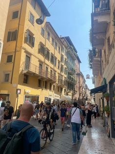 many people are walking down the street in front of some buildings and one person is riding a bike