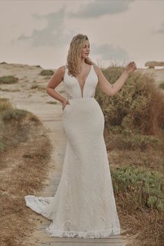 a woman in a white wedding dress standing on a path with her hands out to the side