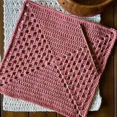 two crocheted dishcloths sitting on top of a wooden table next to a bowl