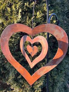 a metal heart hanging from a pole in front of some bushes and trees with the shape of two hearts on it