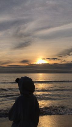 a person is standing on the beach watching the sun go down over the water and clouds