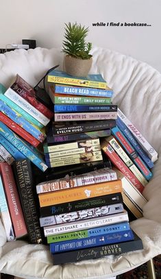 a pile of books sitting on top of a white chair next to a potted plant