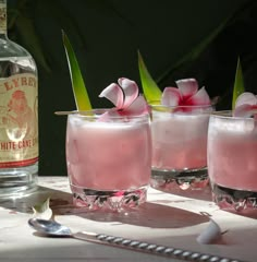 three glasses filled with pink liquid sitting on top of a table next to a bottle