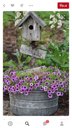 a birdhouse sitting on top of a metal bucket filled with purple flowers