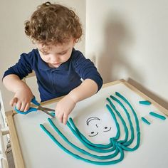 a young boy cutting paper with scissors on top of a white board in front of him