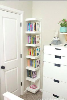 a white book shelf sitting in the corner of a room next to a dresser and door