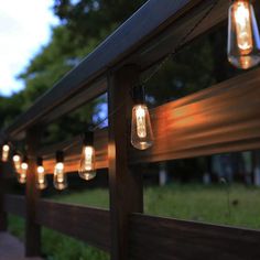 some lights are hanging on the side of a wooden fence with grass and trees in the background