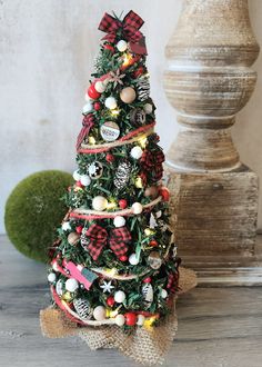 a small christmas tree decorated with plaid ribbon and ornaments is sitting on a wooden table