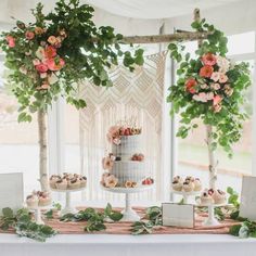 a wedding cake and cupcakes on a table with greenery in the background