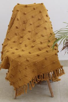 a yellow blanket sitting on top of a wooden chair next to a potted plant