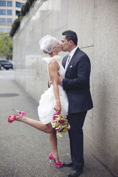 a bride and groom kissing in front of a wall with their feet on the ground