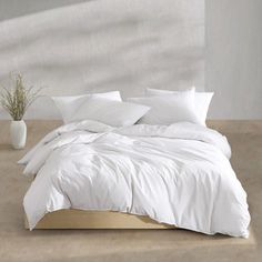 a bed with white sheets and pillows on top of it next to a potted plant