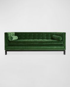 a green velvet sofa with two pillows on it