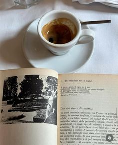 an open book sitting on top of a white table next to a cup of coffee