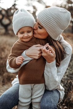 a woman holding a baby in her arms while she is wearing a hat and sweater