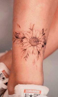 a woman's foot with a sunflower tattoo on the side of her leg