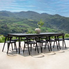 a dining table with six chairs and a vase on it in front of a scenic view