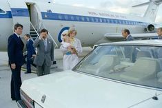 some people are standing in front of an airplane with a baby on the car seat