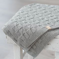 a gray blanket sitting on top of a wooden bench next to a white chair and table