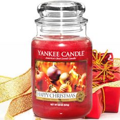 a yankee candle sitting next to a red gift box with gold ribbon around it and a christmas ornament in the background