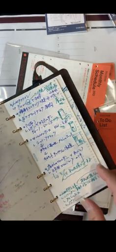 a hand holding a notebook with writing on it next to several folders and papers