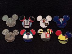 several mickey mouse pins are shown on a black surface, one is wearing a suit and the other has a tie