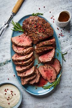 sliced meat on a blue plate with sauce and herbs next to it, surrounded by other food items