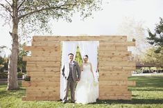 a bride and groom standing in front of a wooden structure with white drapes on it