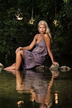 a beautiful woman sitting on top of a rock in the water