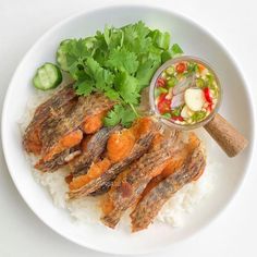 a white plate topped with meat and rice covered in veggies next to a bowl of sauce