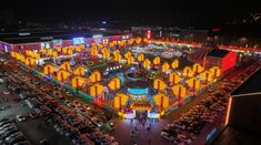 an aerial view of a carnival at night with cars parked in the lot and people walking around